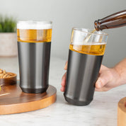 Person pouring cold beer from a bottle into the Elevated Craft Hybrid Pint Glass in gunmetal black finish next to another stainless hybrid pint glass full of cold beer