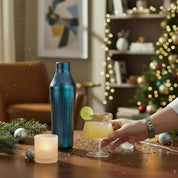 person holding a cocktail that is sitting on a wooden surface with holiday decorations. 
