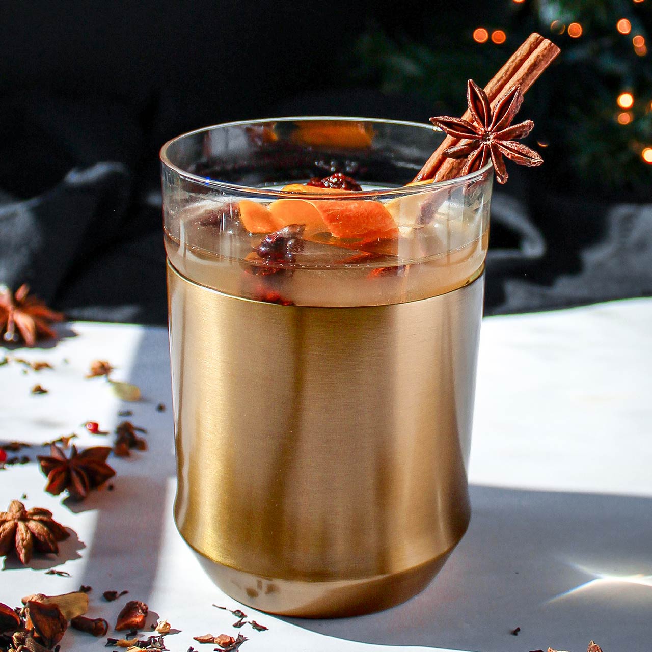 The Elevated Craft Hybrid Cocktail Glass in brushed copper finish filled with a dark orange cockail garnished with a cinnamon stick, muddled rasberries orange peel and star anise balanced on the glass insert rim